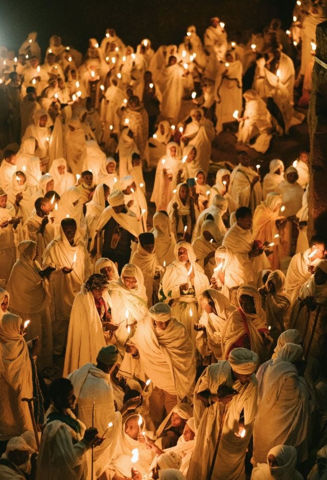 Dozens of Ethiopian people in white robes hold candles during a Christmas celebration