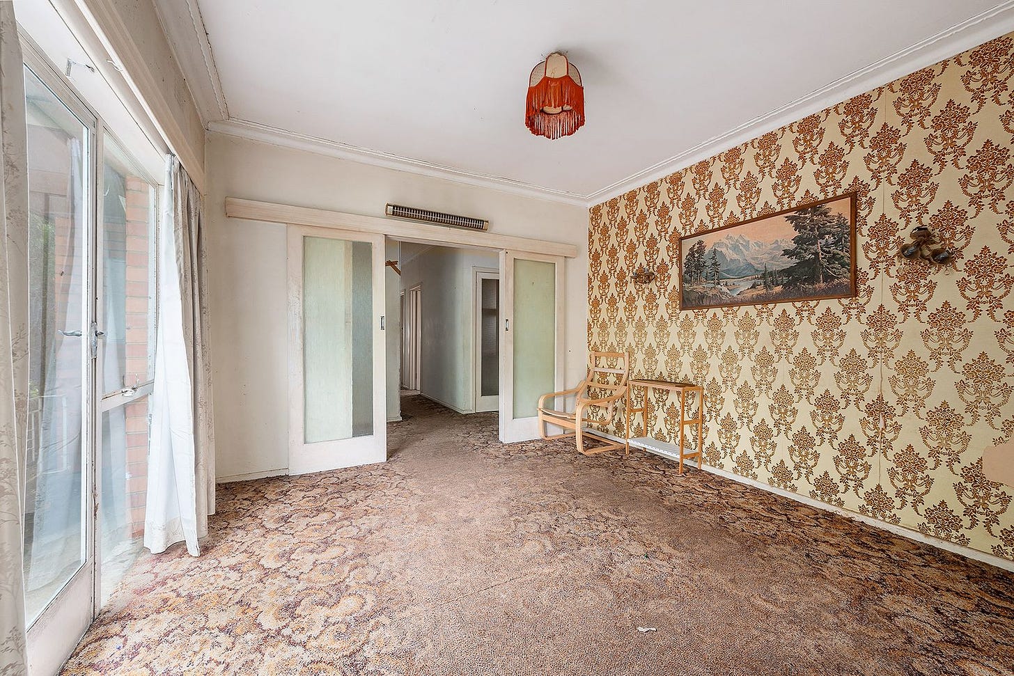 Loungeroom with ugly brown decorative wallpaper, a door, a horrible 80s lamp and brown carpet.