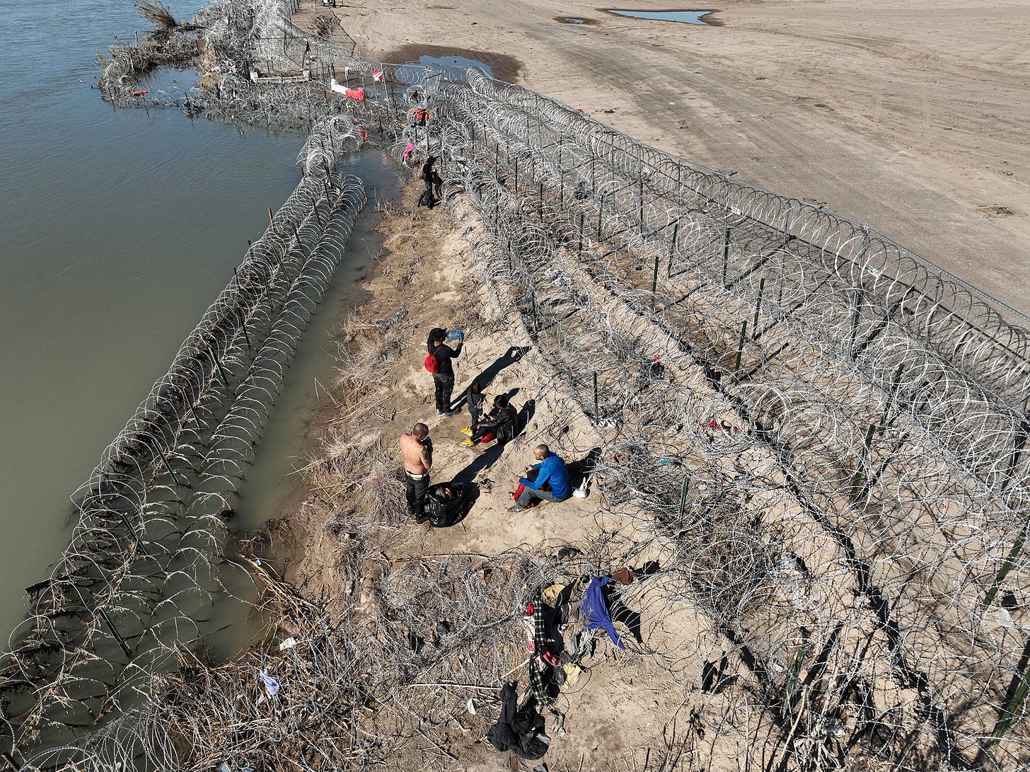 An aerial view of migrants walking along razor wire after crossing the Rio Grande into the United States on January 28...