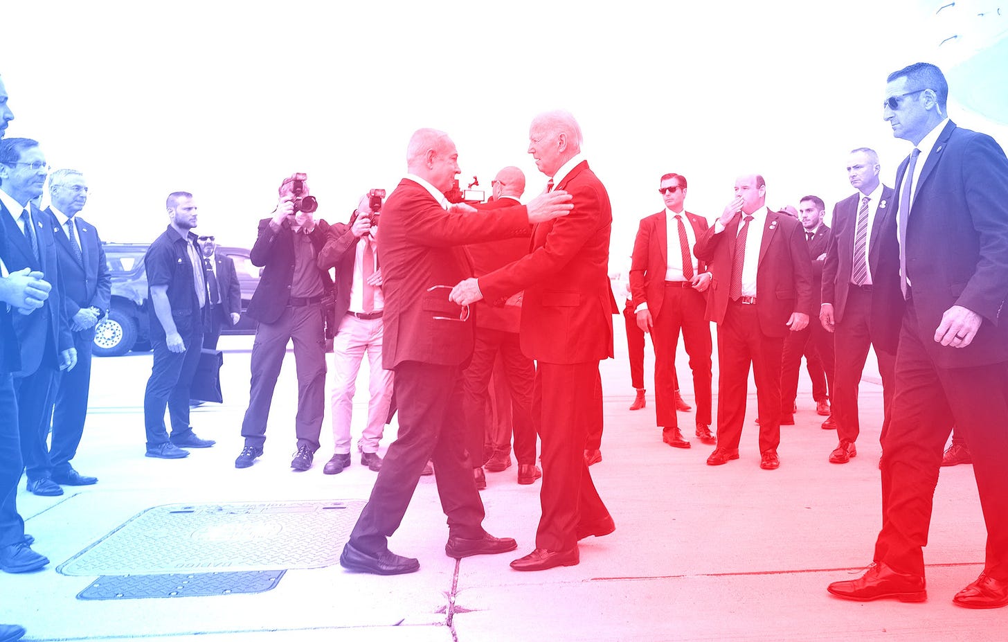 The Israeli Prime Minister Benjamin Netanyahu greets President Joe Biden on a tarmac in Tel Aviv. There is a redandblue...