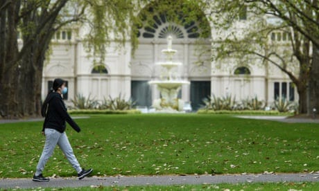 A person wearing a face mask walks through Carlton Gardens in Melbourne