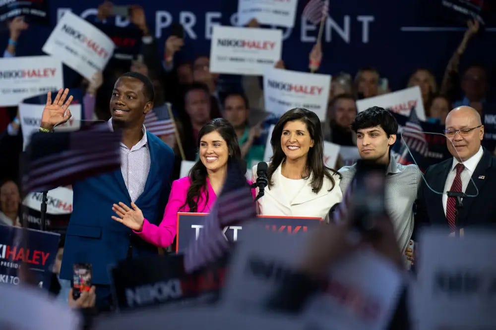 Nikki Haley at a rally flanked by her family and surrounded by campaign signs.