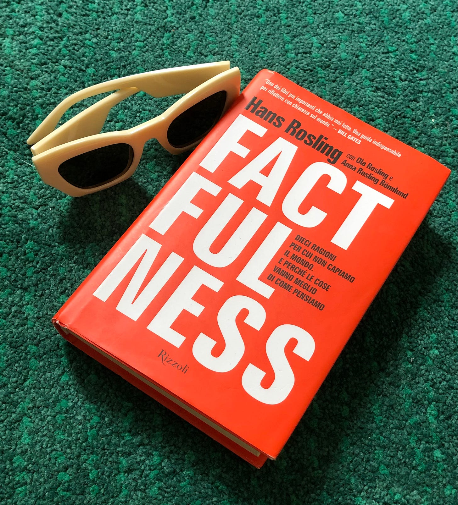 Il libro Factfulness di Hans Rosling su un tappeto verde per fingere di essere su un prato, con i miei occhiali da sole con montatura bianca a fianco.