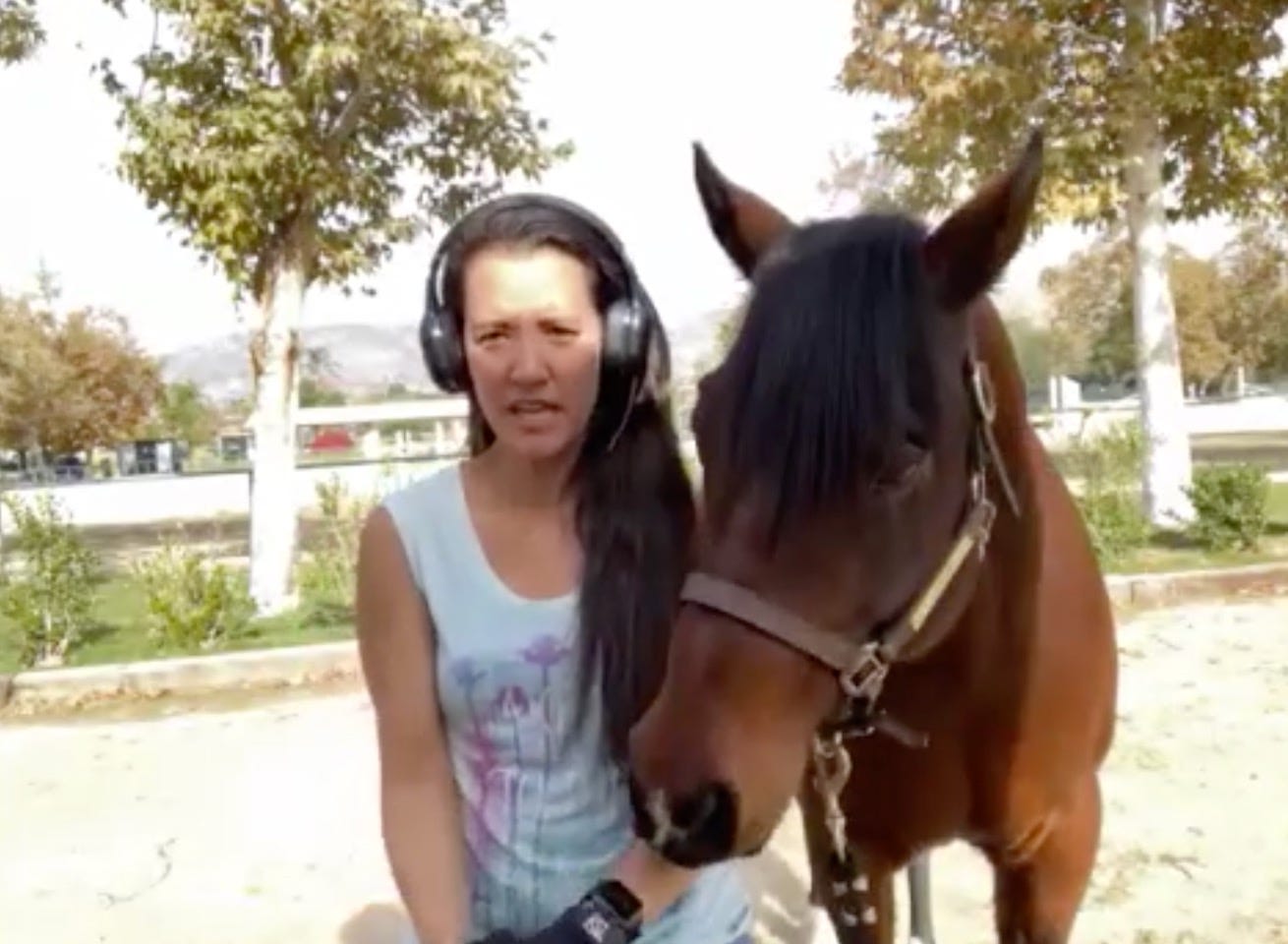 woman in headphones with a brown horse standing nearby