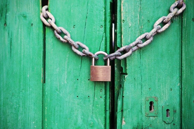 A padlock in the locked position tying a chain together over a green door.