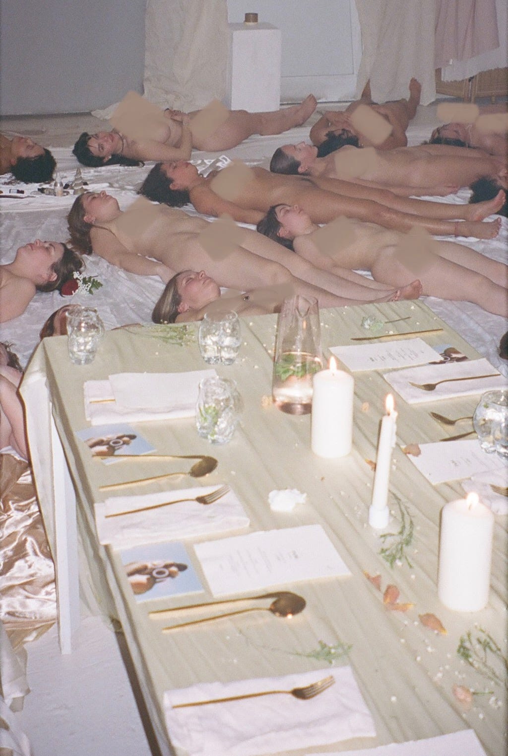 Nude people doing a meditation lying on the floor next to a beautiful laid dinner table at Looni and Füde event