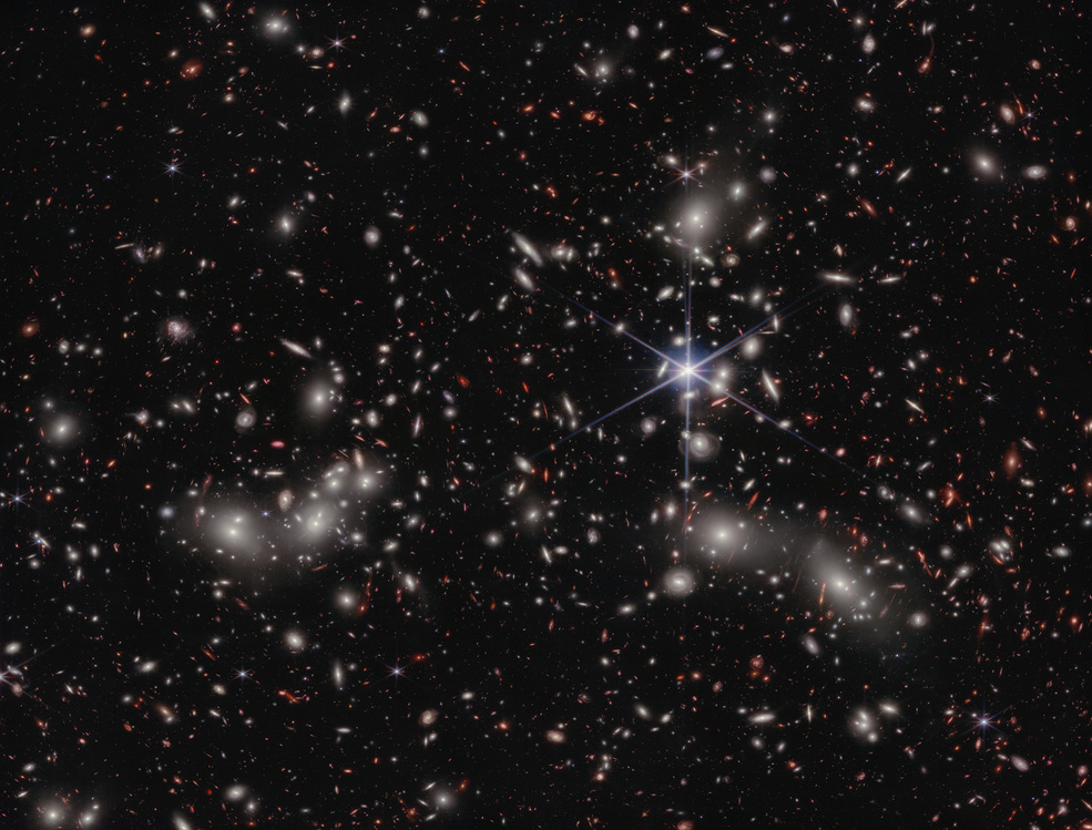 A crowded galaxy field on a black background, with one large star dominating the image just right of center. Three areas are concentrated with larger white hazy blobs on the left, lower right, and upper right above the single star.