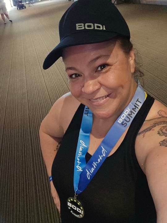 a smiling and energetic woman in workout clothes with a medal around her neck