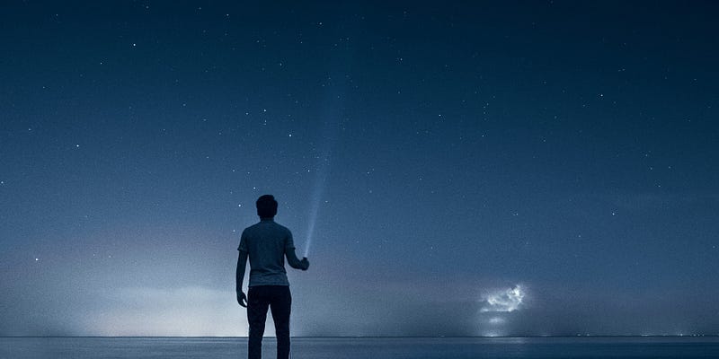A person holding a flash light and pointing into the night sky and the horizon