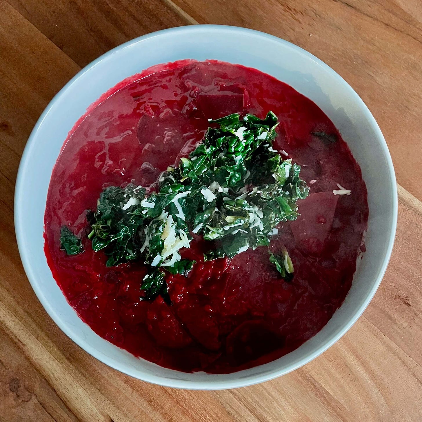 A bowl of bright red beetroot risotto with a deep green lacinato kale on top.