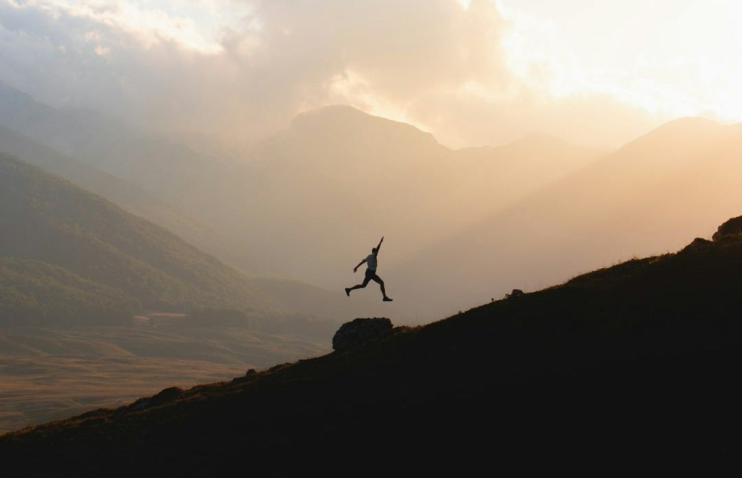silhouette of person jumping on mountain during daytime silhouette of person jumping on mountain during daytime