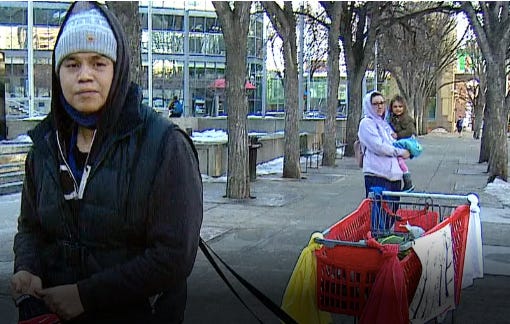 Vee Duncan, wearing a hoodie and a grey toque, is harnessed to a shopping cart they are pulling down a street near the legislature in Edmonton. 