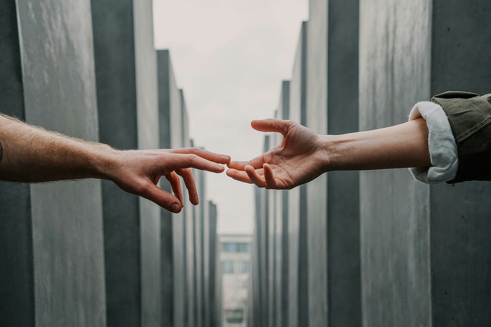 A pair of hands reach out for one another against the backdrop of Jewish memorial markers of the Holocaust. A pair of hands reach out for one another against the backdrop of Jewish memorial markers of the Holocaust.