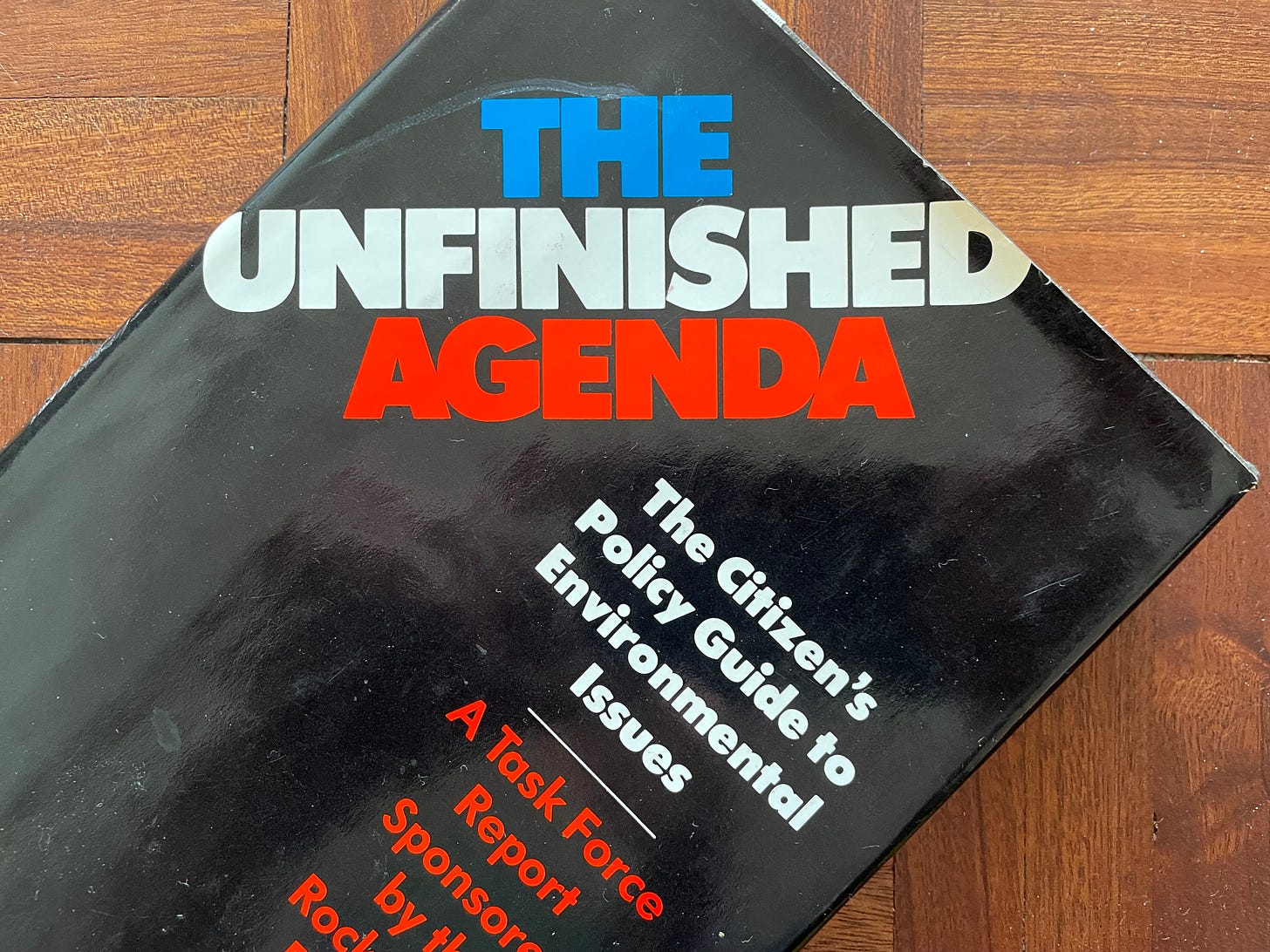 Photo of a copy of The Unfinished Agenda with a black gloss cover and the words written in blue, white and red