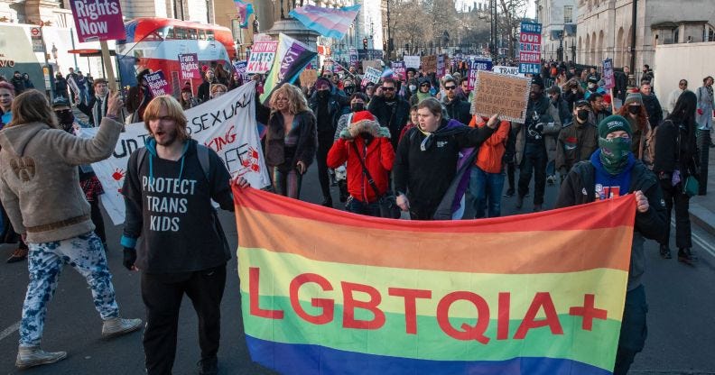 Protestors march through a street with pro-LGBTQ+ flags.