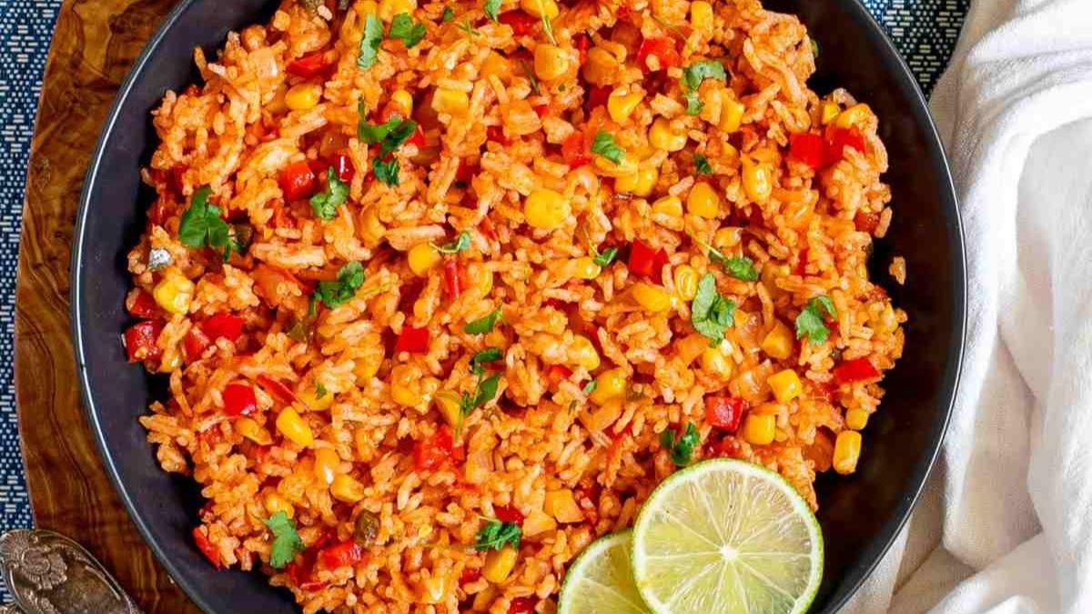 A vibrant plate of mexican rice garnished with fresh cilantro, featuring mixed vegetables like corn and red bell peppers, accompanied by a slice of lime on the side.