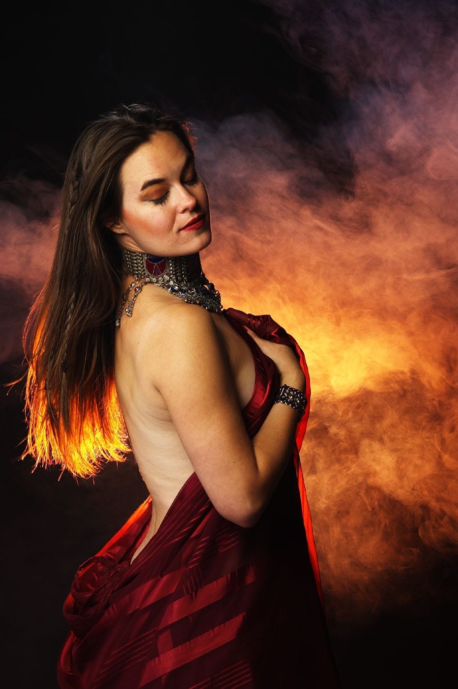 The author, eyes closed amidst glowing, fiery smoke, draped in a veil and an ornate metal choker