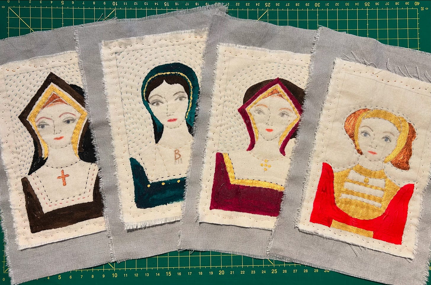 Small stitched portraits of four Tudor women, stitched on to grey linen backgrounds. They represent the first four queens of Henry VIII and are depicted in clothes and headgear appropriate to each. The pictures are head and shoulders in the style of sixteenth century portraits.