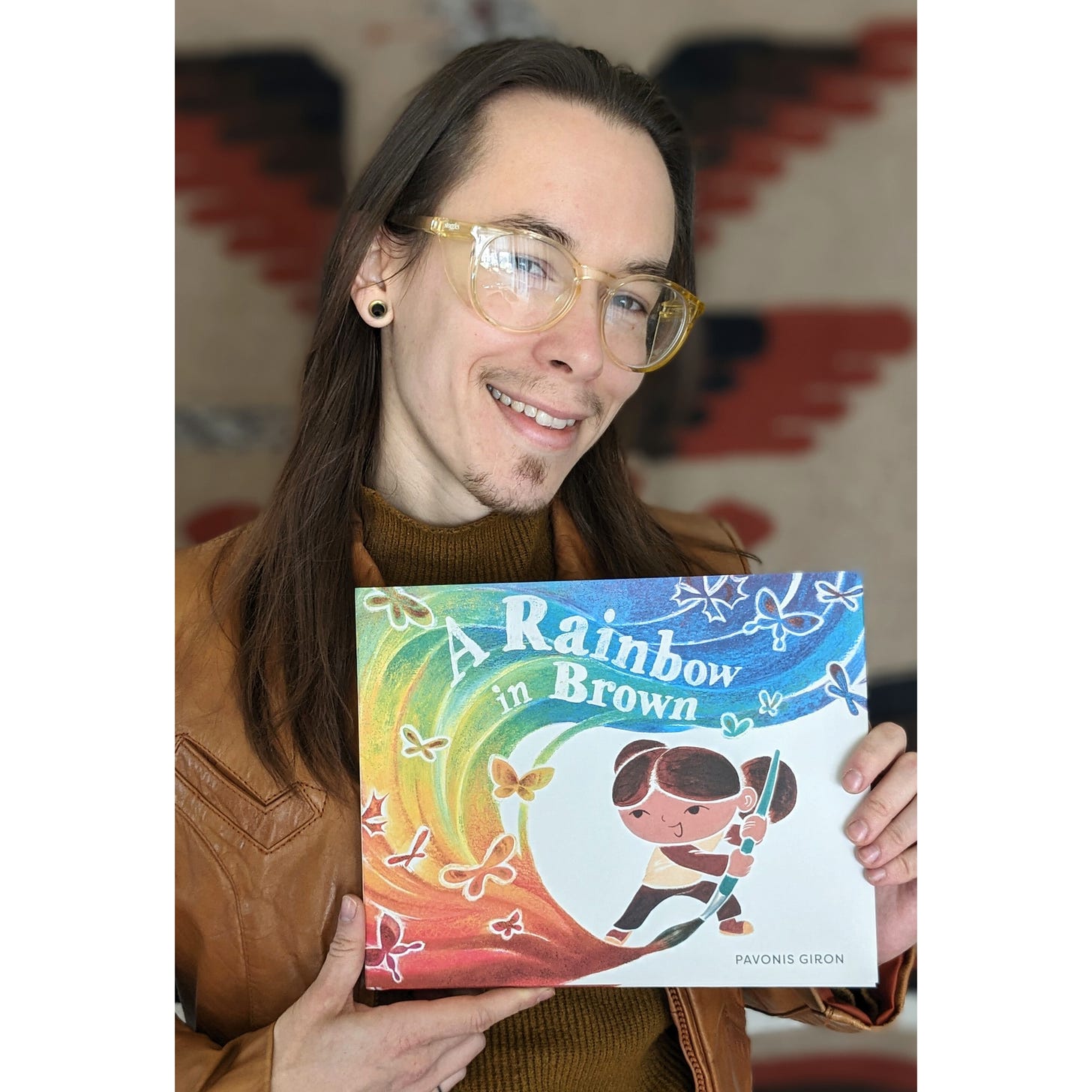 Author-illustrator Pavonis Giron holding their debut picture book, A RAINBOW IN BROWN