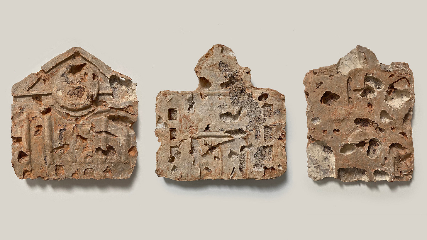 A series of three sculptures in rough earth tones side by side on a wall