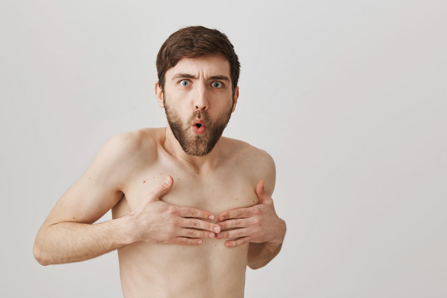 A comedic stock photo of a bare man covering his nipples and looking offended