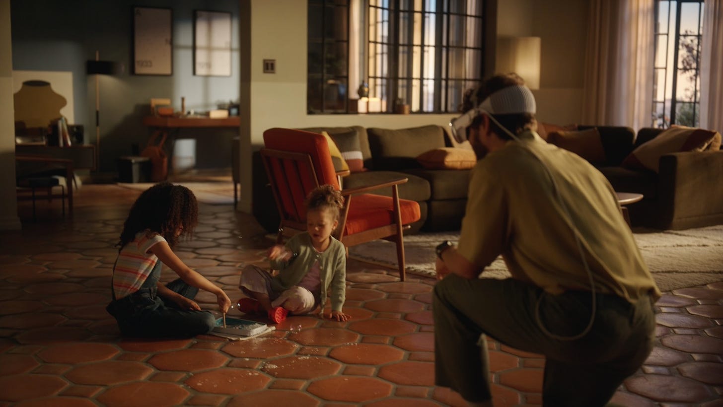 Two children playing in a living room, with a man wearing the VisionPro headset uses it to record video of them.