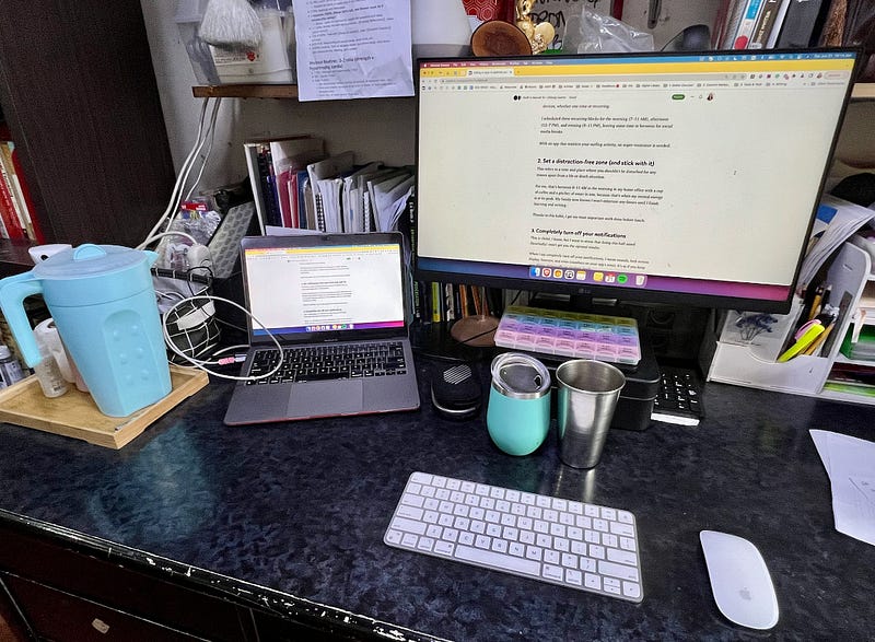 Home office work station with a laptop, computer, pitcher of water and a cup of coffee