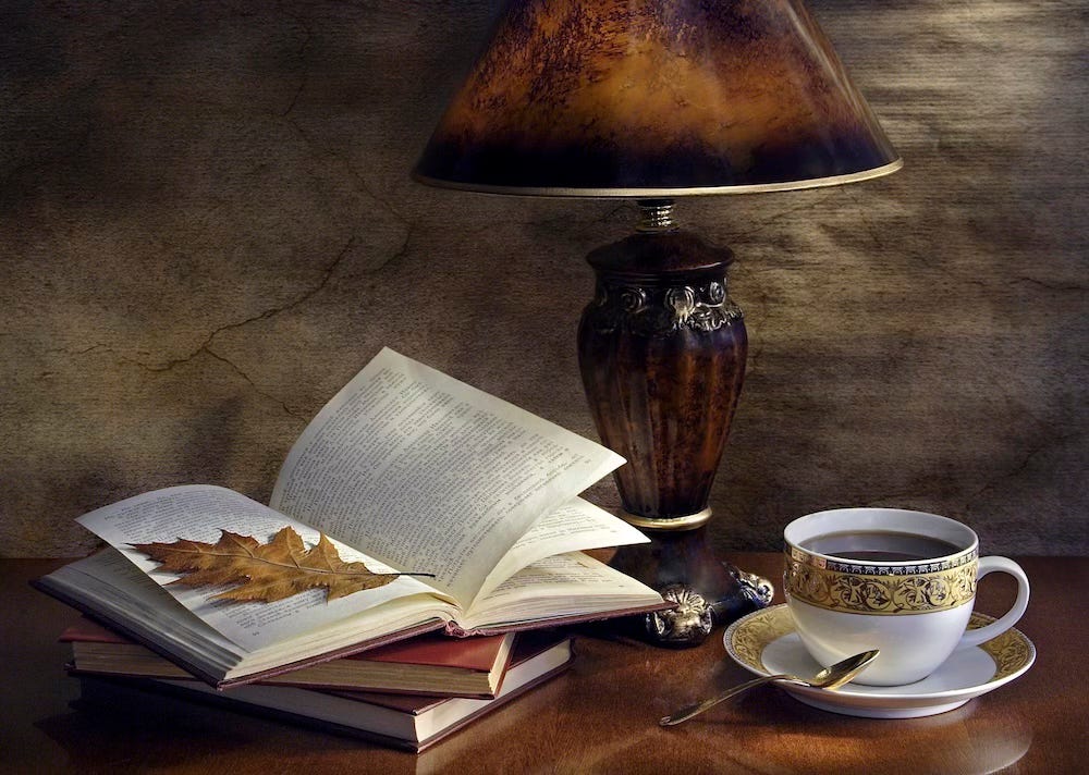 Book with a leaf on it, sitting on a table by a lamp and a cup of tea