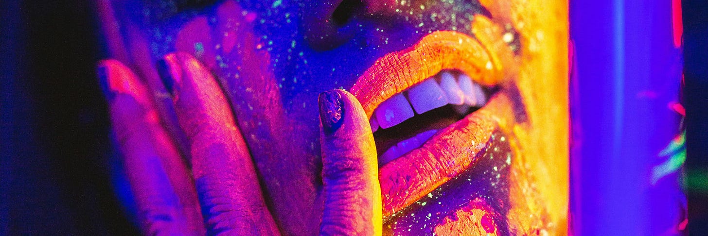 A face in neon colours, with fingers resting against the cheek, mouth slightly open revealing teeth.