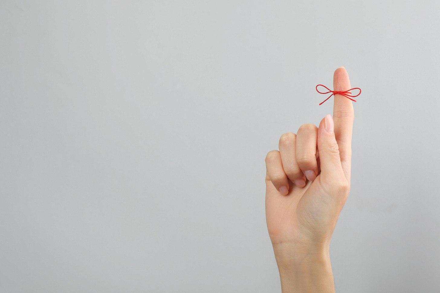 "Don't forget" - a woman's hand with a red string tied around the index finger as a reminder