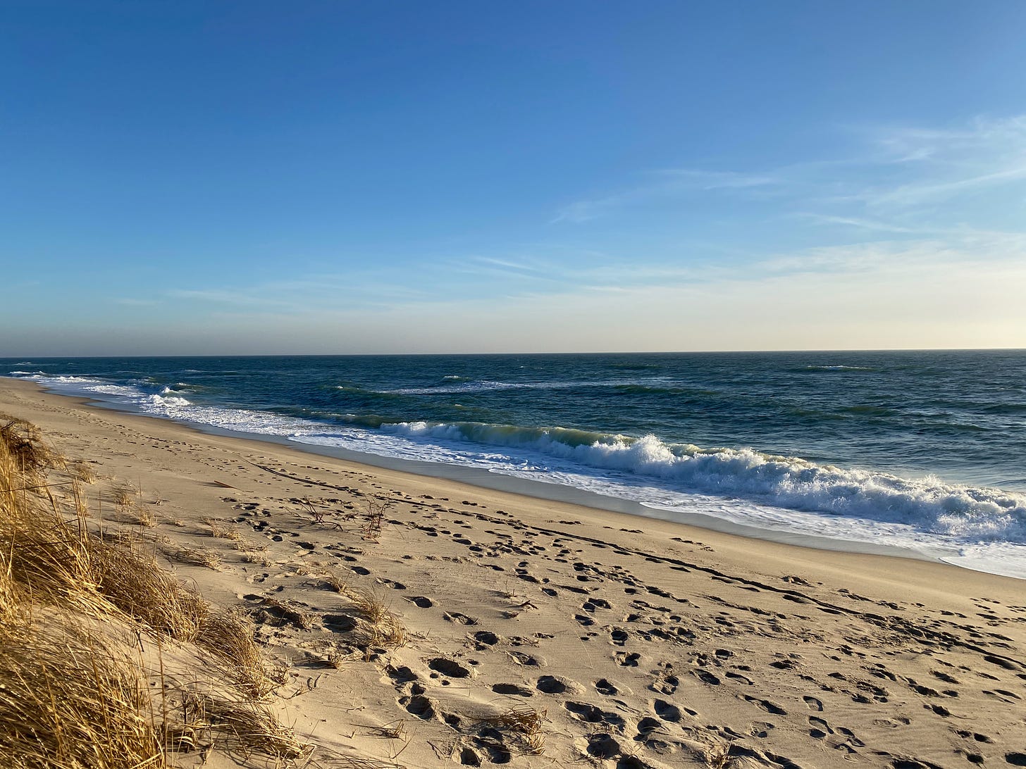 View of a beach with crashing waves under a bright blue sky.