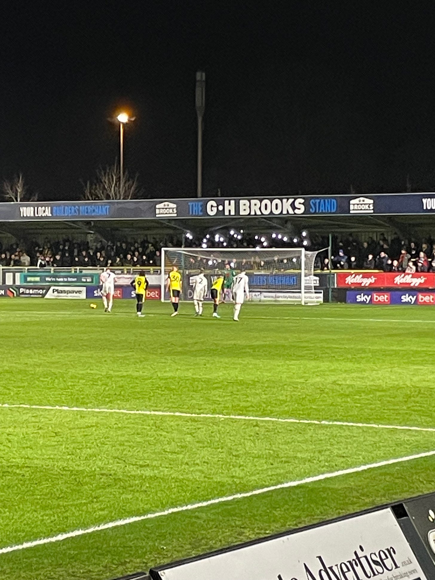 A penalty about to be taken, phones held aloft behind the goal.