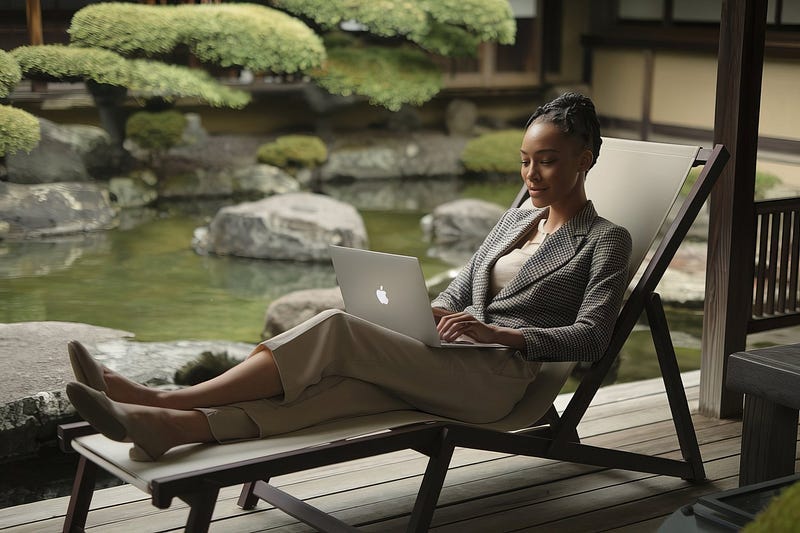 African woman sitting on a deck chair in a Japanese garden typing on her MacBook Pro.