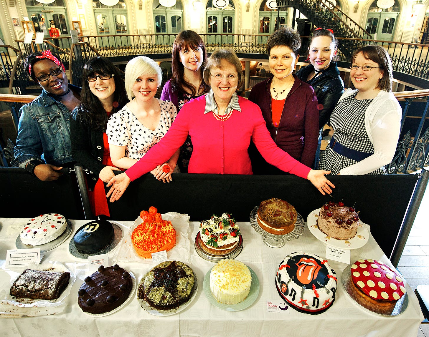 Group of people around a table full of cakes. 