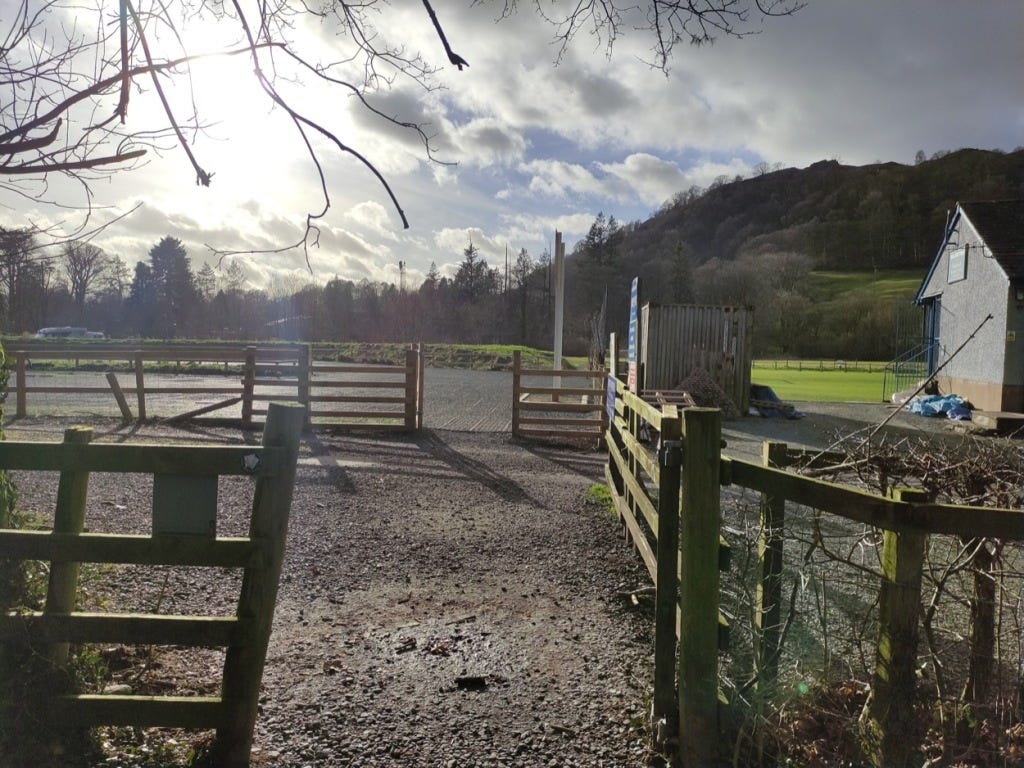 A muddy path through gates, with the local football club building on the right.