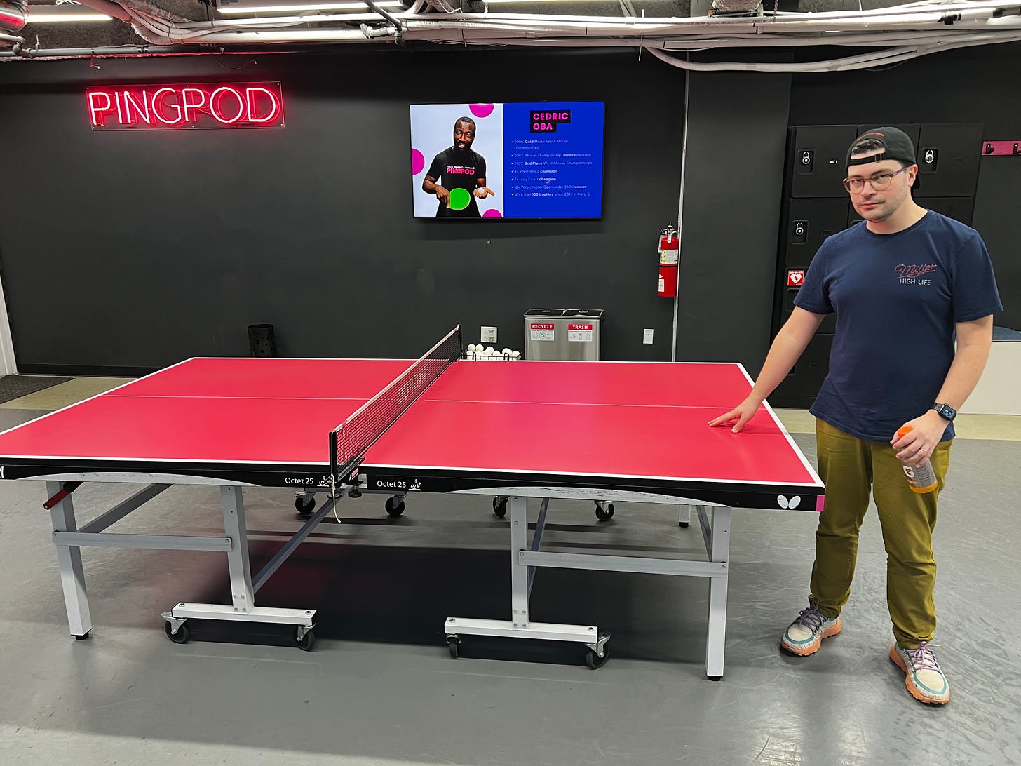 Man stands, touching ping pong table in a PingPod location.