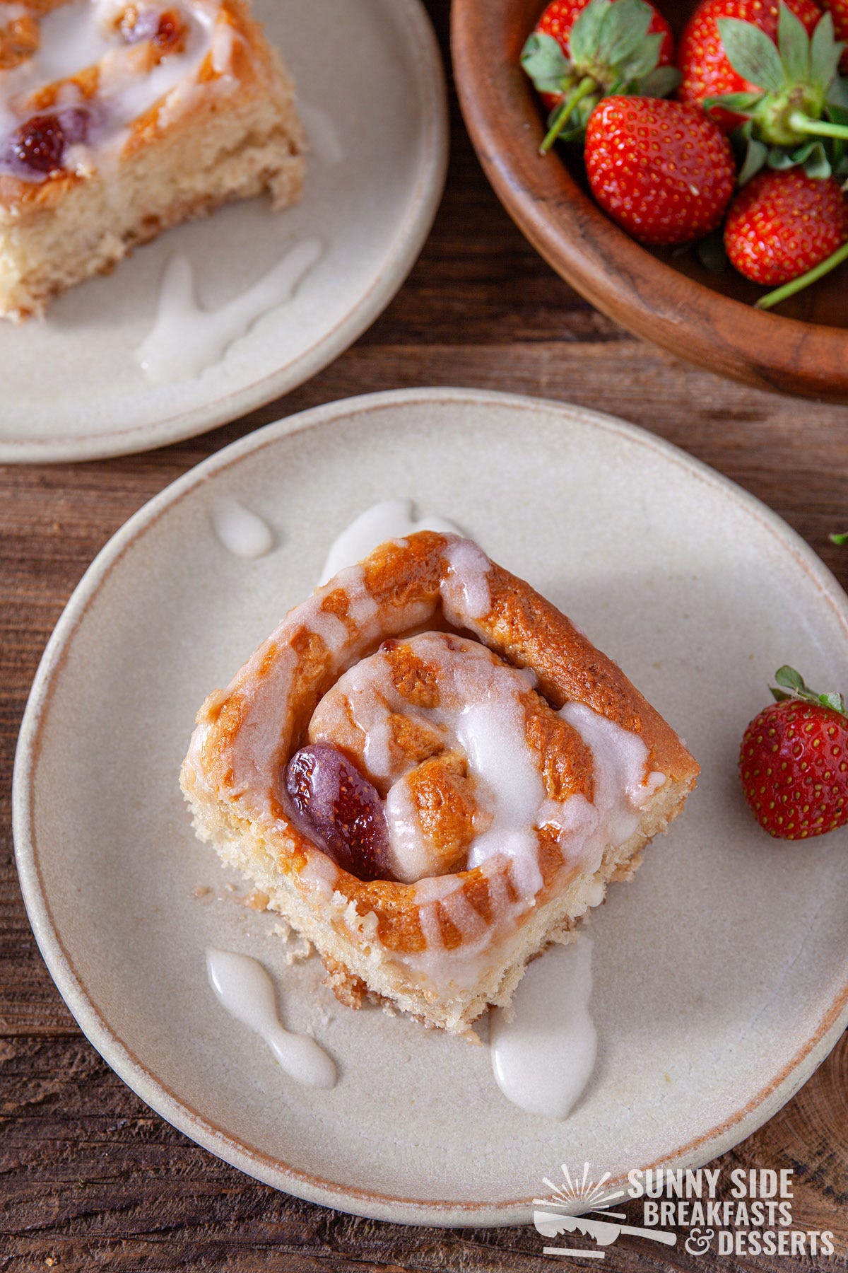 A strawberry maple bun on a plate next to fresh strawberries.