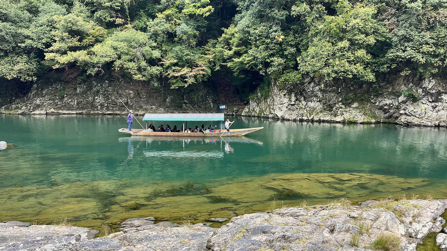 The Katsura River through the Arashiyama Mountains with a traditional wooden boat full of tourists. 