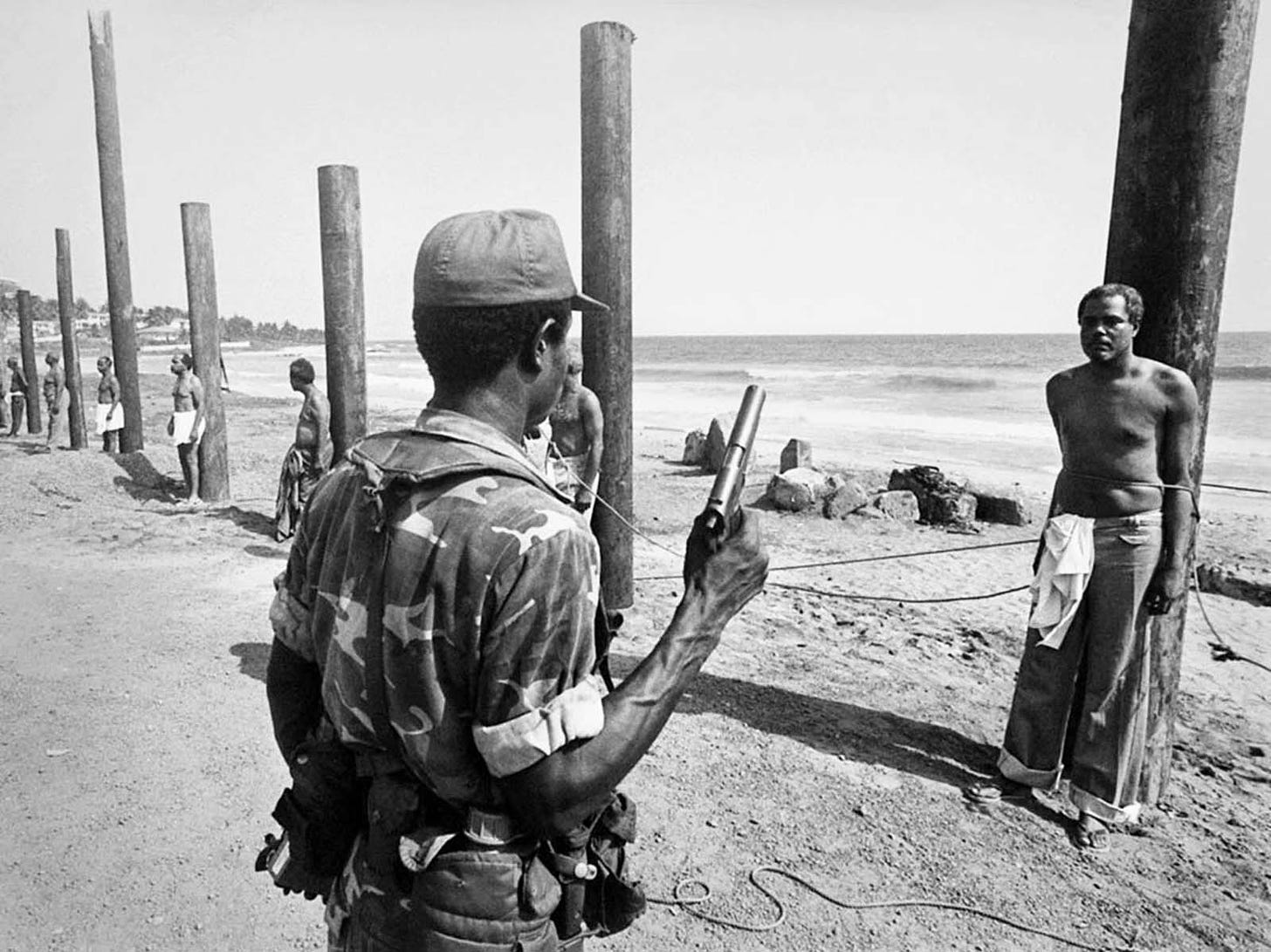 A Liberian army soldier stands ready to execute a former cabinet minister following the 1980 coup. The minister in the photo: Cecil Dennis.