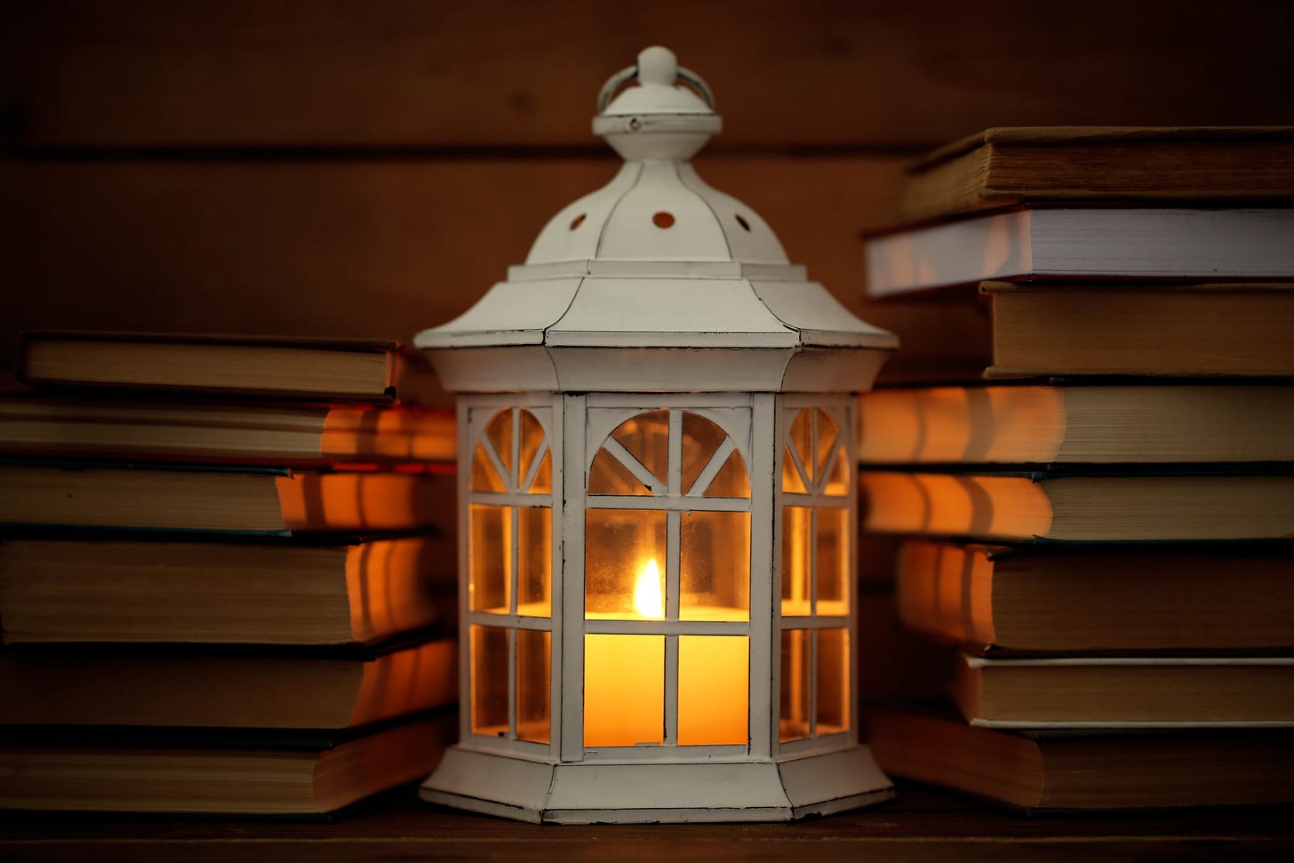 White wooden lamp between two stacks of book. There’s a lit candle inside the lamp. 