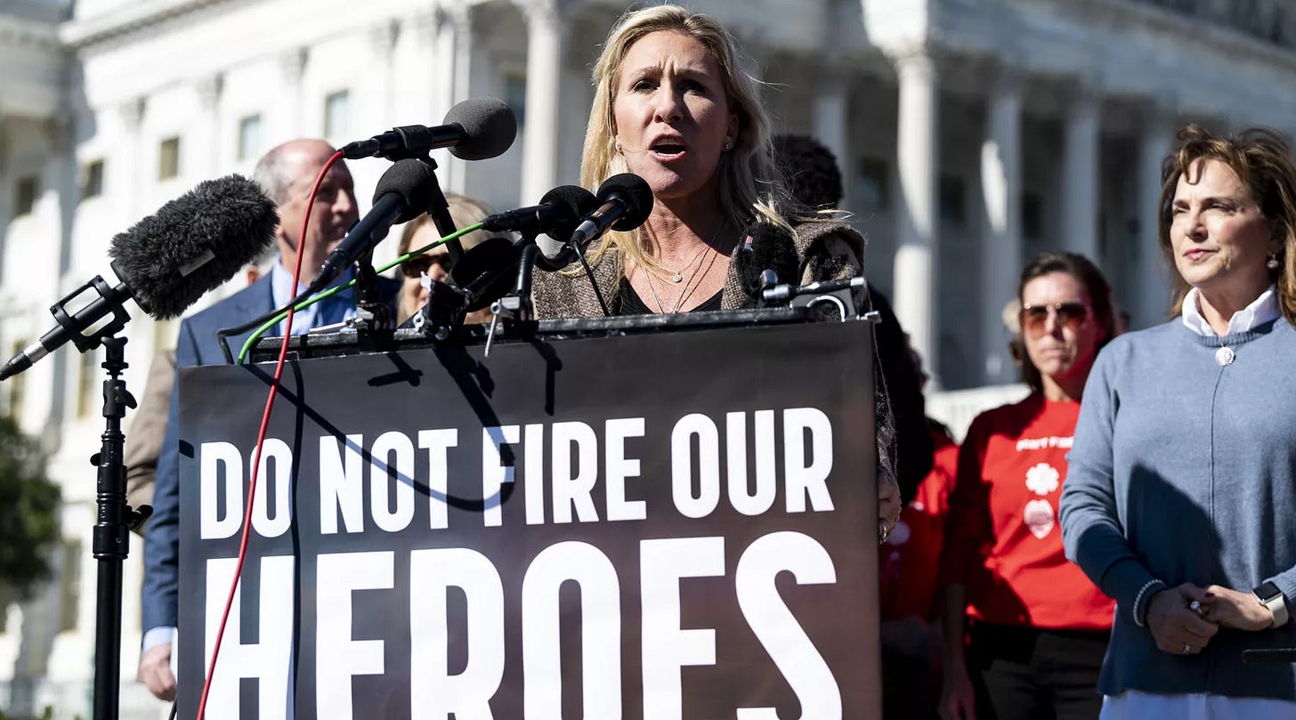 MTG speaking in front of congree at a podium with "do not fire our heroes" written on it.