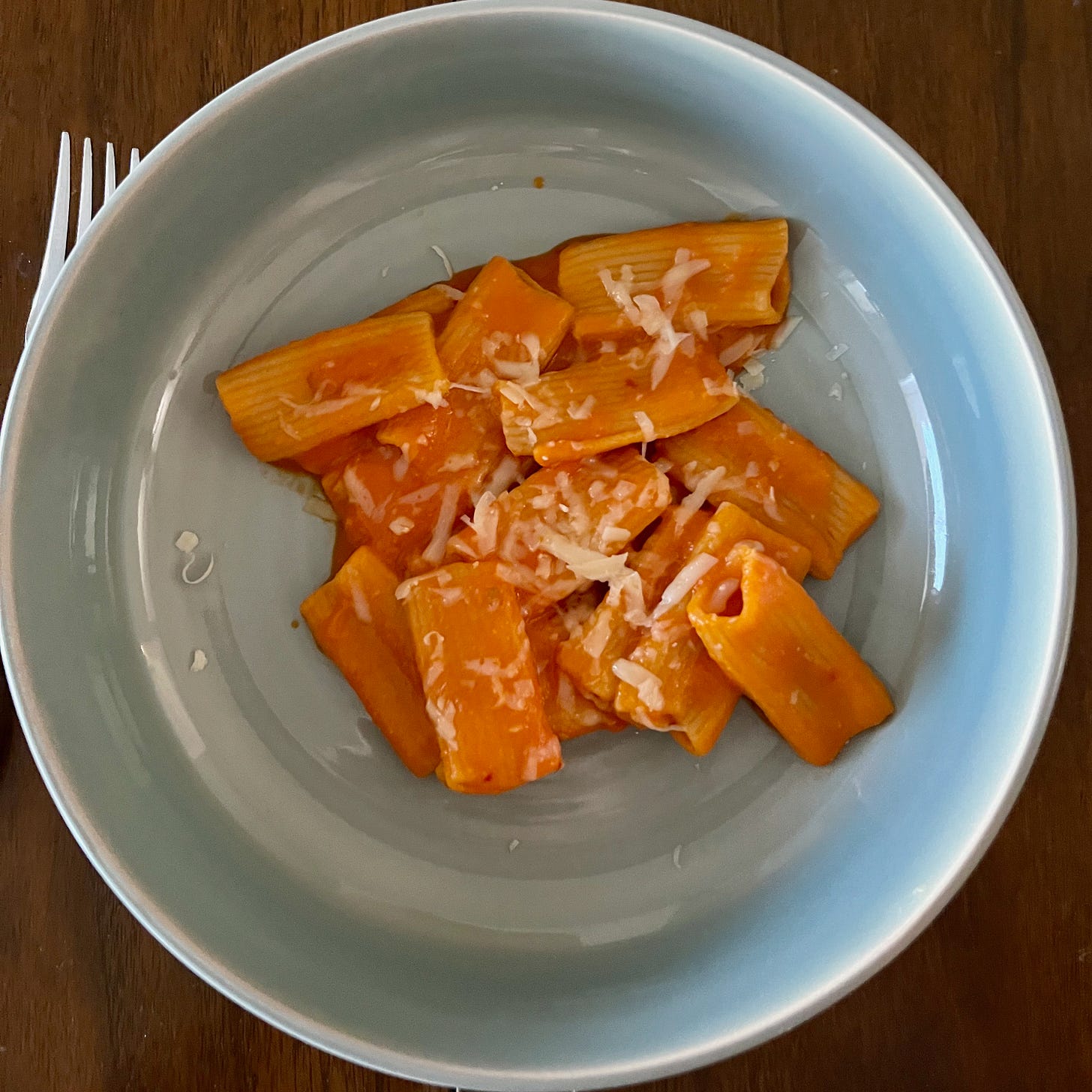 a blue bowl with rigatoni in vodka sauce with cheese on top