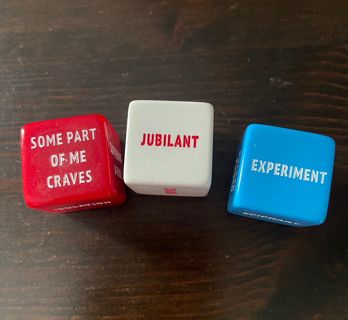 Picture of three dice, a red one that says: SOME PART OF ME CRAVES, a white one that says: JUBILANT, and a blue one that says: EXPERIMENT