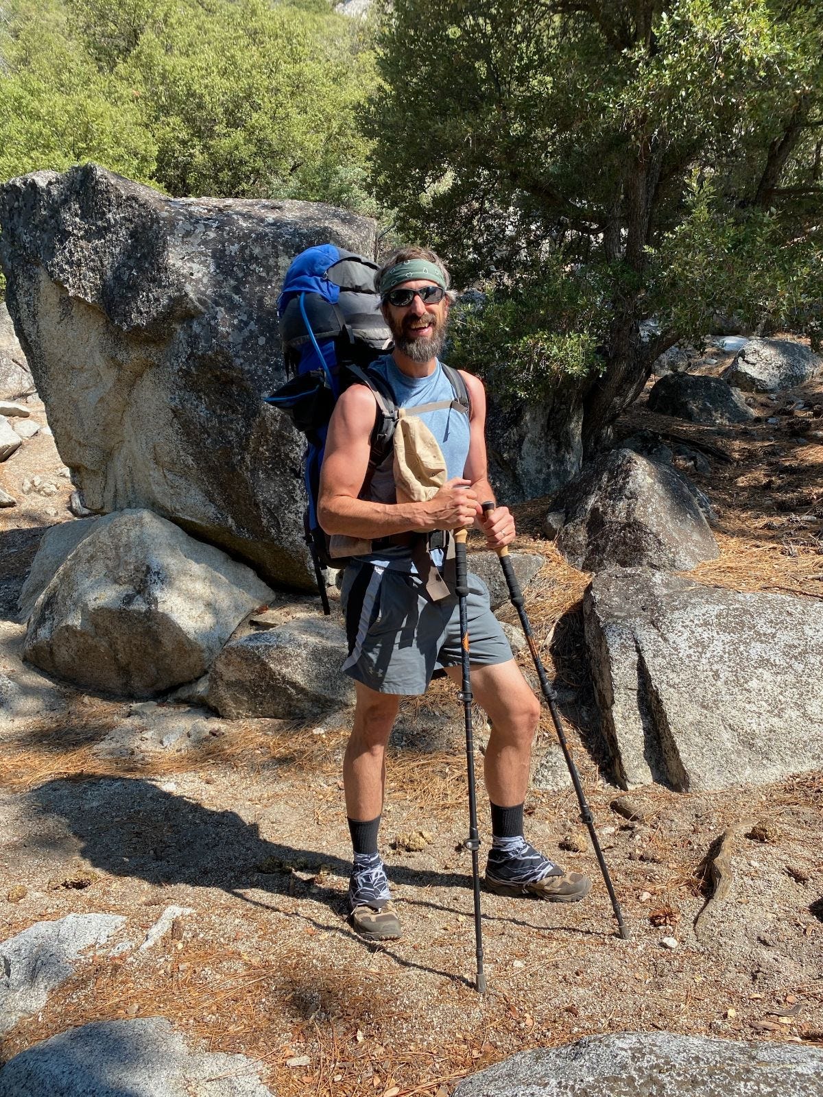 Scott standing at the start of his trail with a full backpack, hiking sticks, and a smile.