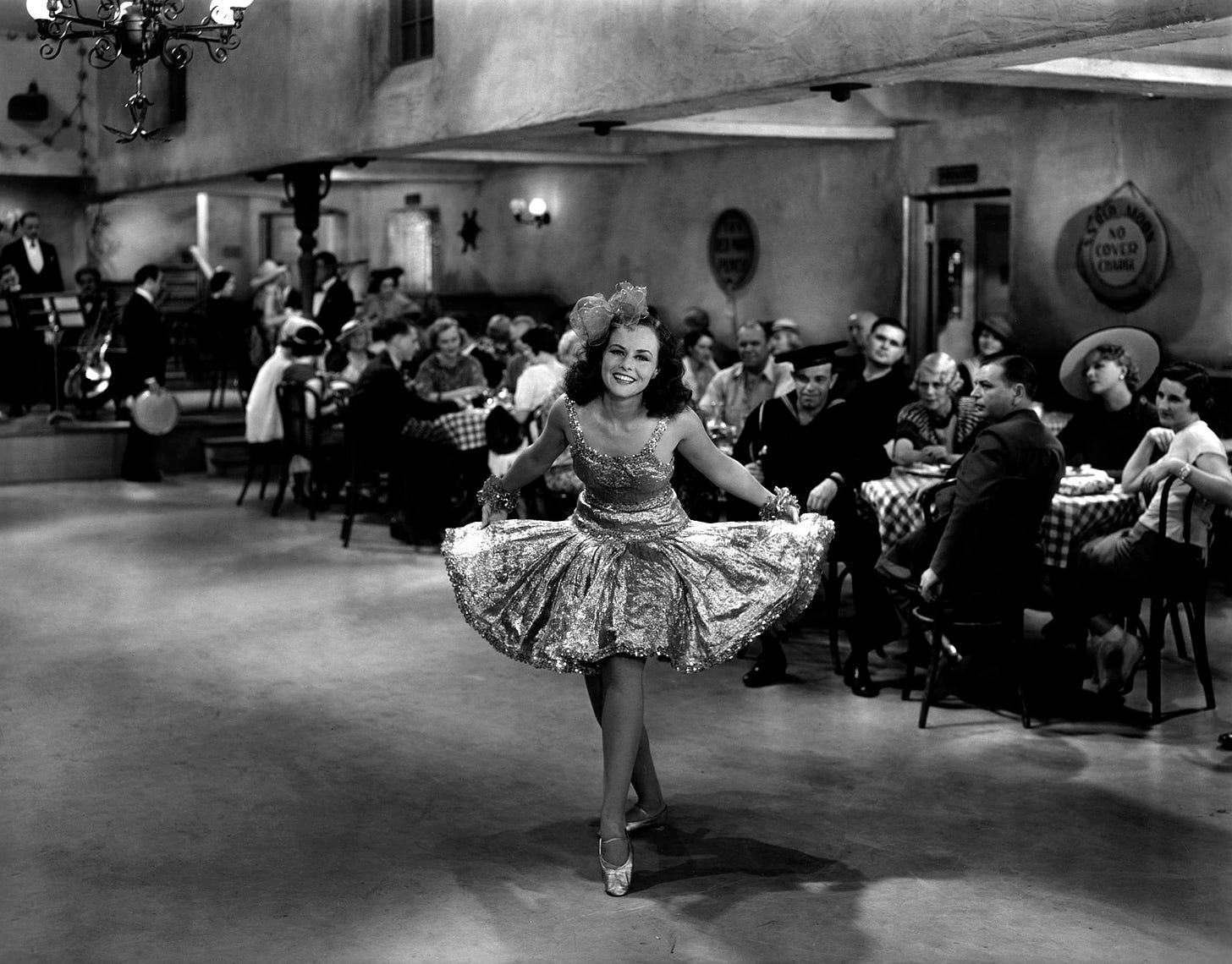 Paulette Goddard curtsies and smiles in a fabulous short gold dress on the dancefloor in the cafe she works in. Behind her an audience of diners at their tables