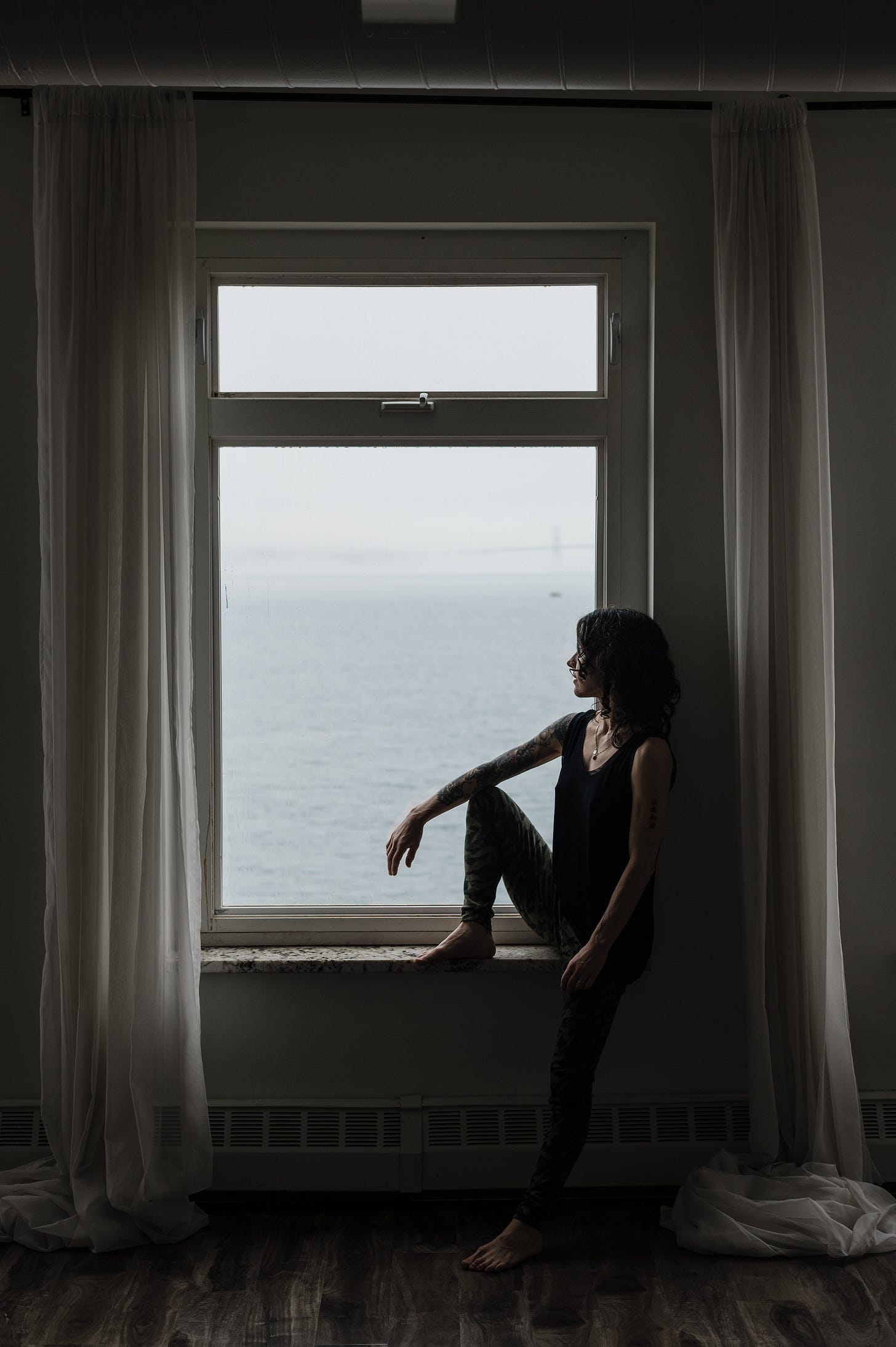Author seated in a large window looking out over the water in Nova Scotia