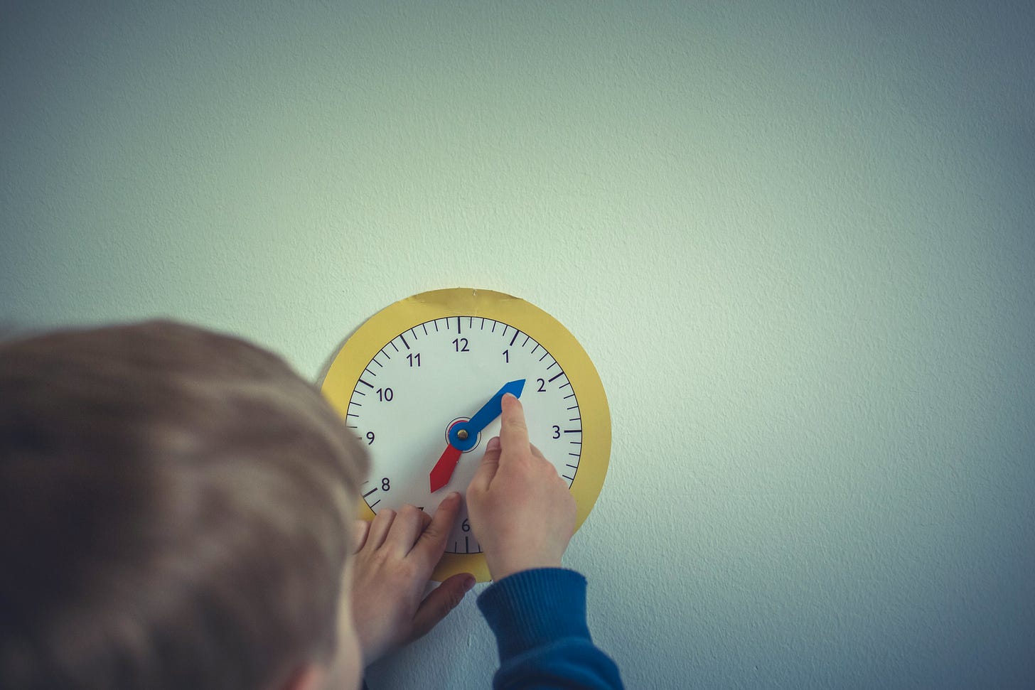A photo of a young child moving the hands on an analogue clock to learn how to tell the time