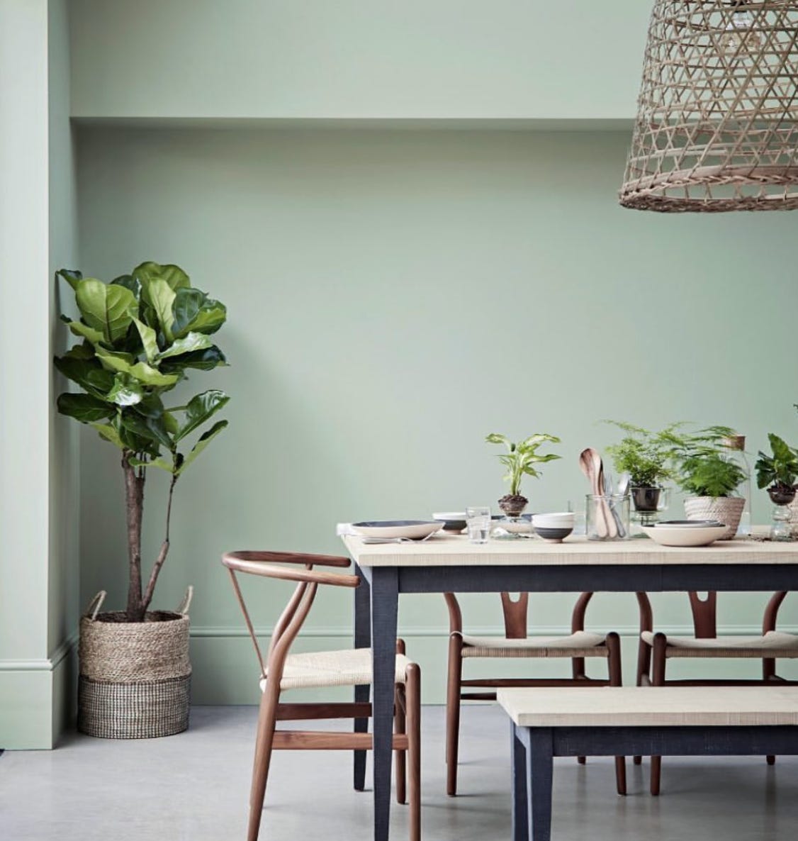 Soft green painted wall with wooden dining table positioned off centre