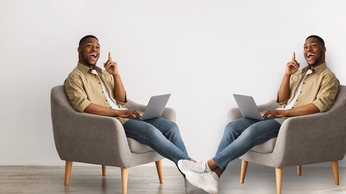 Two identical men sitting in chairs with laptops, pointing upwards and smiling at each other.