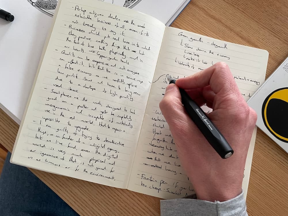 Photo of my hand holding my fountain pen over my notebook with hand written notes in black ink